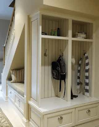 A small bench is installed underneath a stair case along with a small cubby for jackets and backpacks