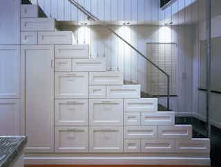 A white stair case with abstract shelving for storage built in underneath the stairs