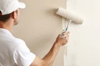 A photograph of a Homefix employee painting a living room wall in white