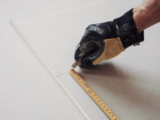 A hand cutting through measured drywall