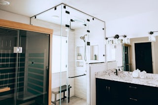 A bathroom remodel with a wooden sauna and a walk in, glass shower with a rain fall shower head in Colorado Springs