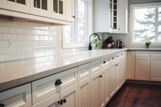 A photograph of white custom cabinets installed with a kitchen remodel that has a white tile splash wall and custom wooden floors