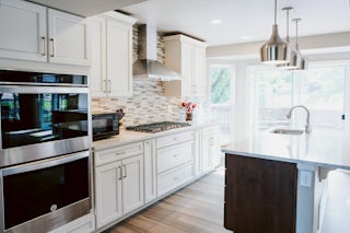 A wide angle photo of a newly remodeled minimal kitchen with white cabinets, countertops and stainless steel appliances