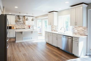 A wide angle photo of a newly remodeled minimal kitchen with white cabinets, countertops and stainless steel appliances facing the eastern morning light in Colorado Springs