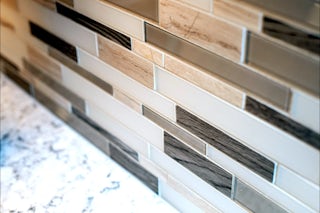 A photograph of a grey and tan tiles on a splash wall of a newly remodeled kitchen